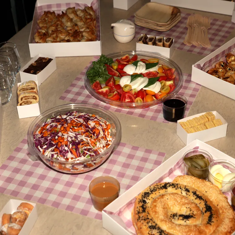 מגשי אירוח של ROMY'S מלמעלה: קפרזה, סלט כרוב, קופסאות מאפים ובורקס על נייר משבצות ליילך